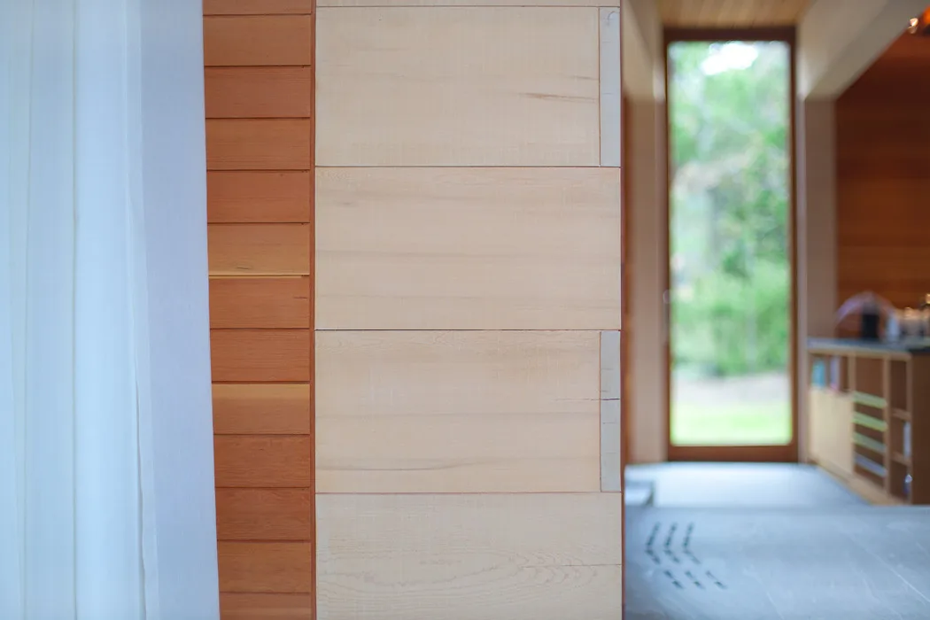 Interior detail of light wood paneling and a window opening with a garden view at the East House by Peter Rose + Partners.