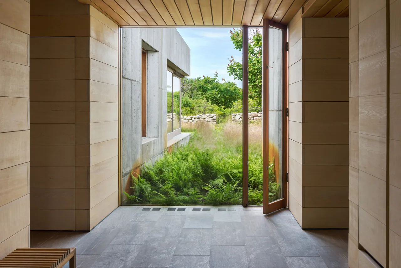 Entryway of East House features wood paneling and opens through a glass door to a landscaped garden courtyard.