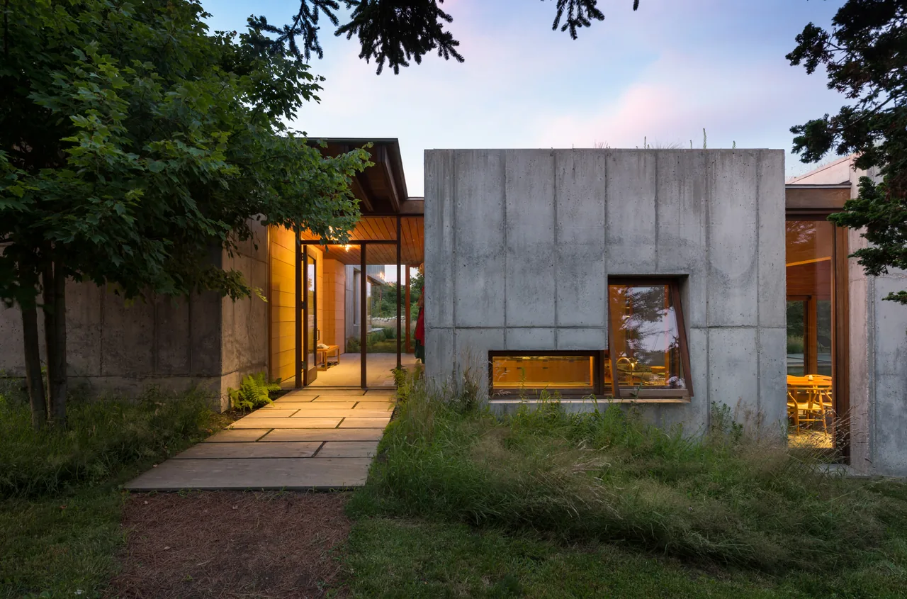 East House features exterior concrete walls with distinctive angled windows and an illuminated entry path through landscaping.
