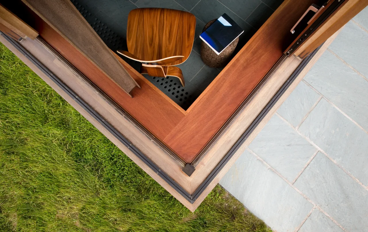 Corner of an interior room with wood and dark tile floors next to grass and stone exterior patio at Vineyard Residence.