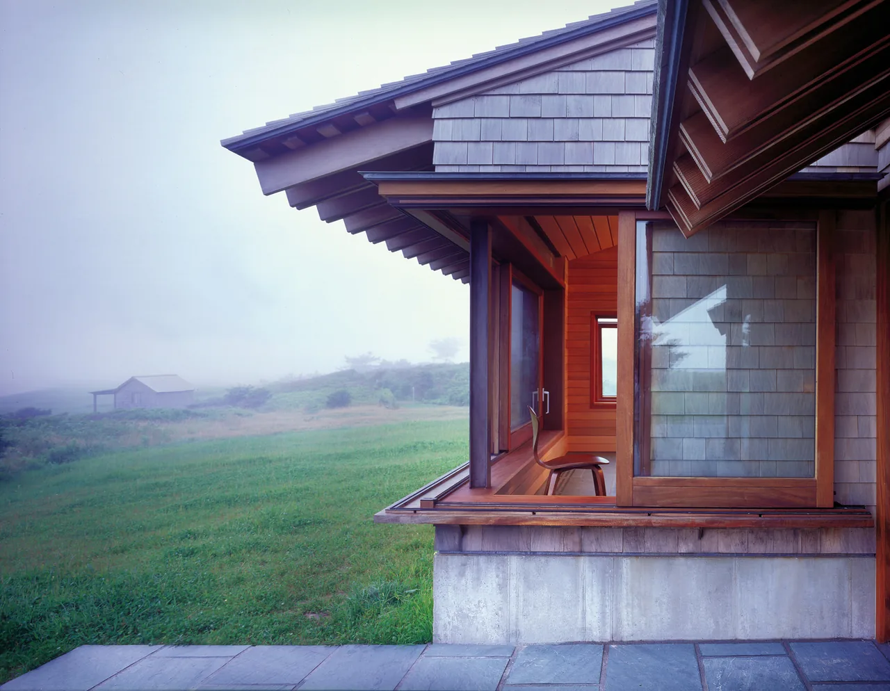 The Vineyard Residence corner with wood-framed windows and shingle siding overlooking foggy green fields.