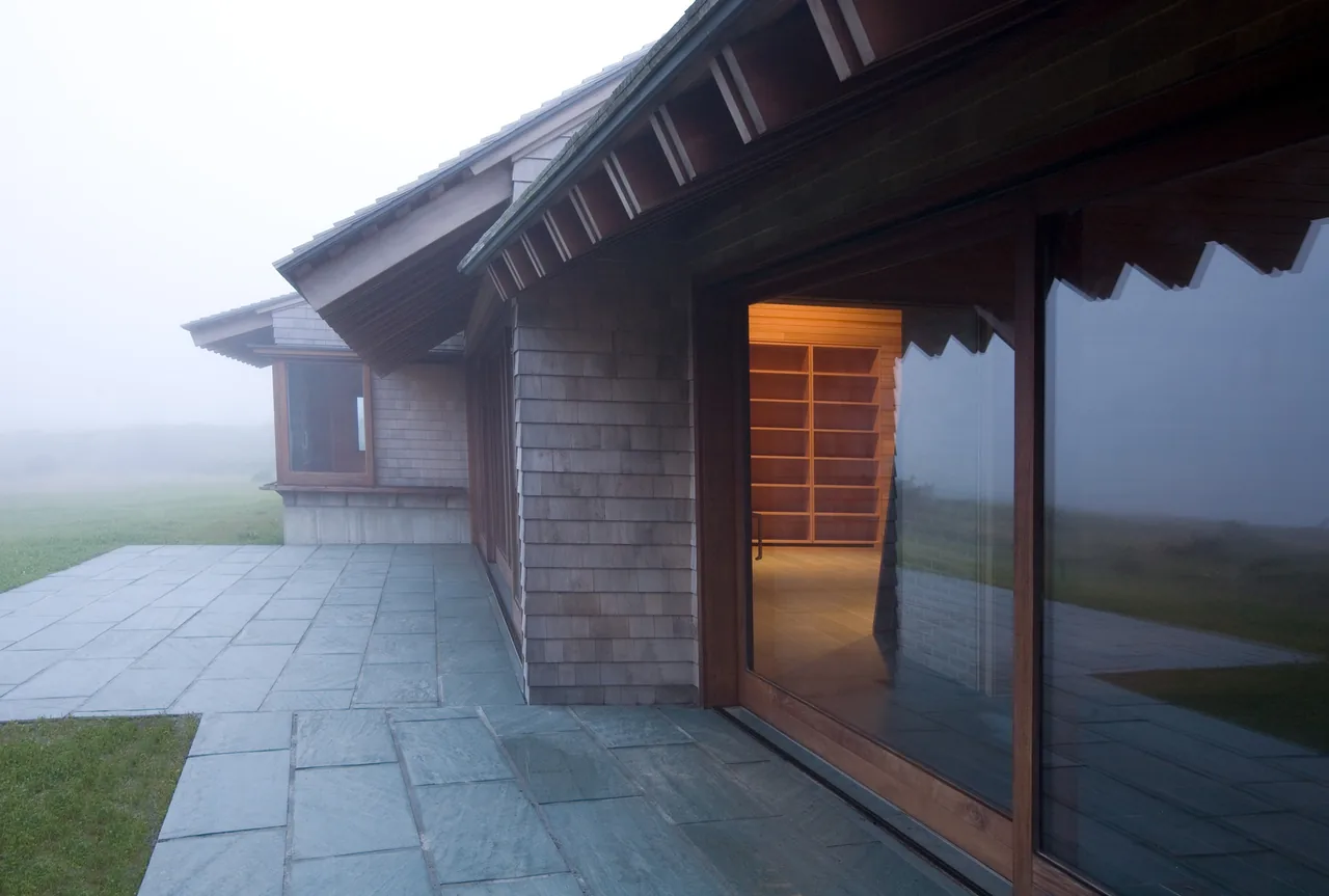 Vineyard Residence features shingle siding and a stone patio with large wood-frame windows reflecting the foggy landscape.