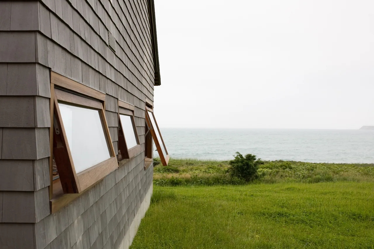 The Vineyard Residence features shingle siding and wooden awning windows facing the ocean.