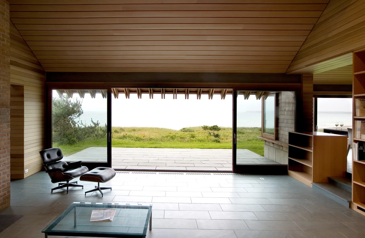 Living room of Vineyard Residence with wood ceiling, stone tile floor, and large wood-framed sliding glass doors to patio.