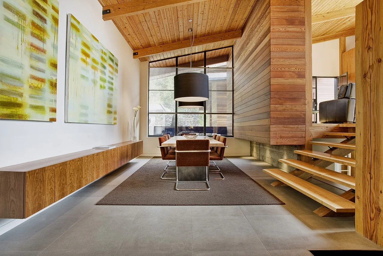 Dining area with floating wood console along one wall and open riser wood stairs adjacent.