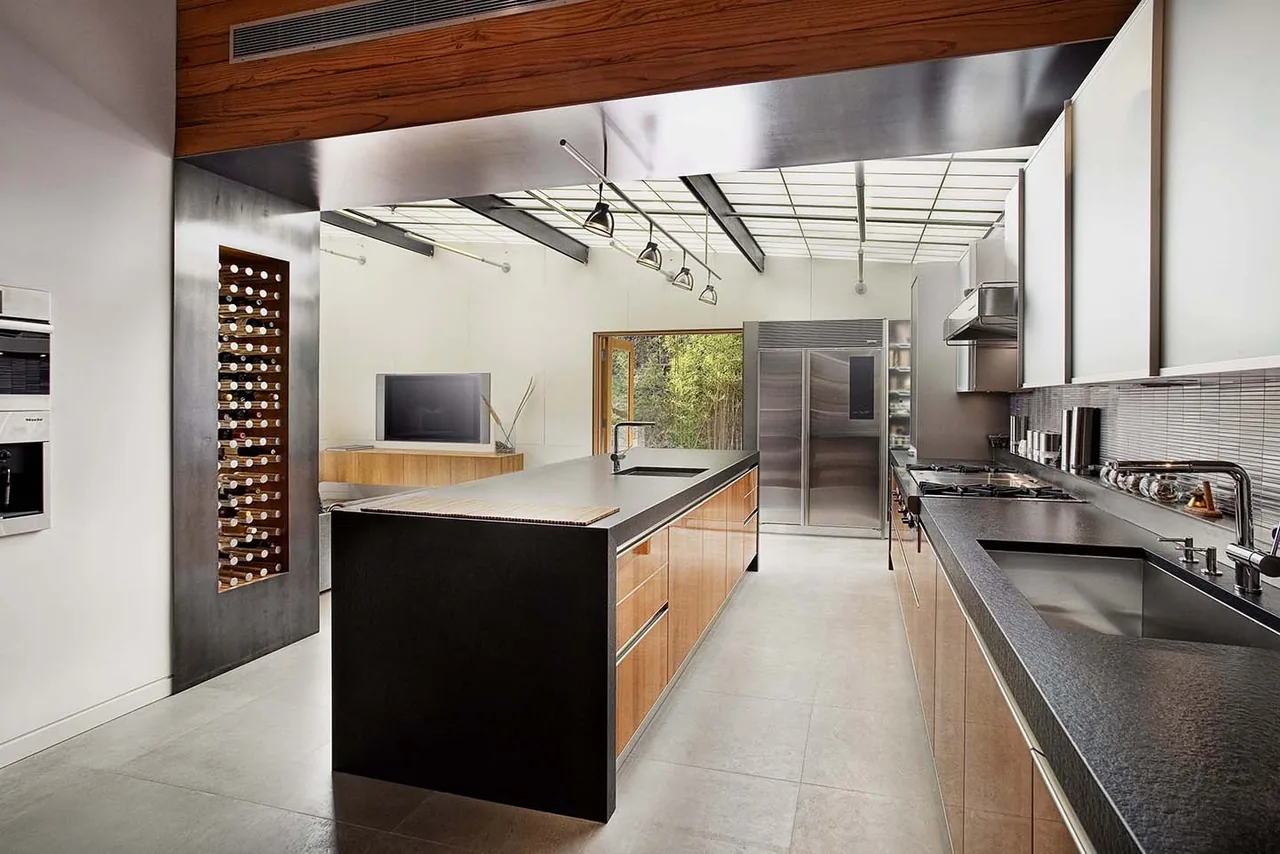 The Lovell Residence kitchen features a streamlined design with black countertops, wood cabinets, and a translucent ceiling above the island.