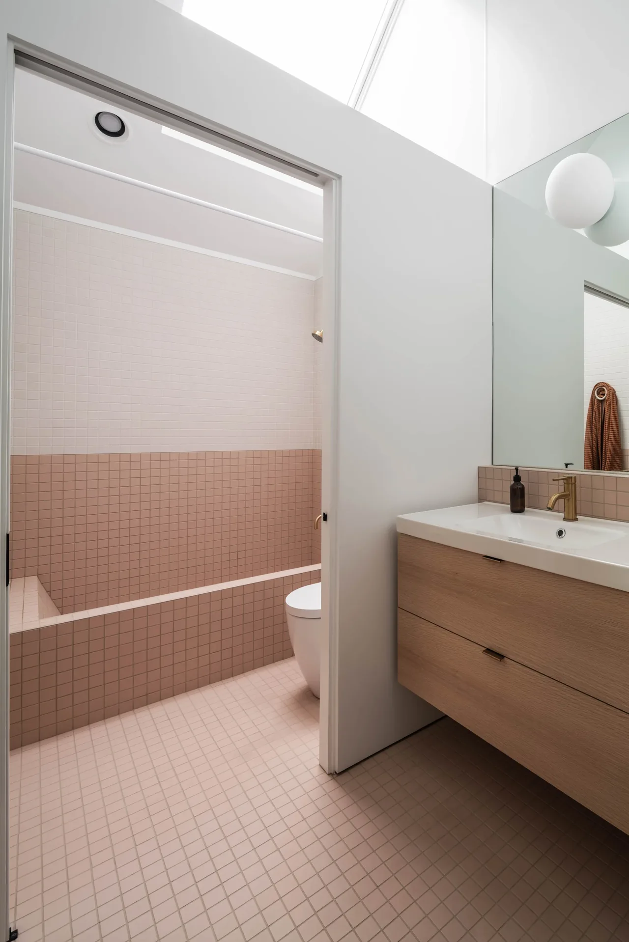 This modern bathroom features two-tone pinkish tile, a wood vanity, and brass fixtures at Oak Avenue House by ras-a, inc.