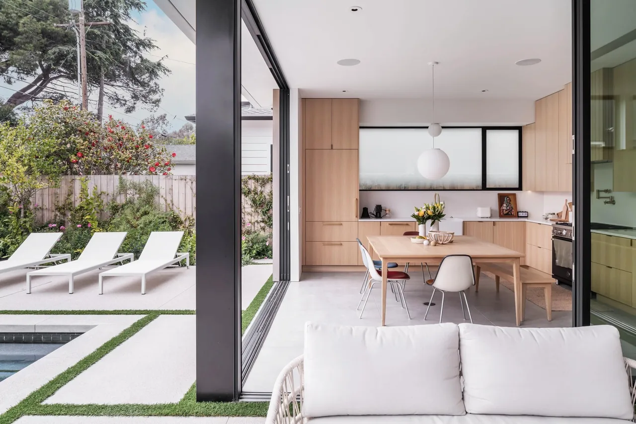 The Oak Avenue House kitchen and dining area with wood cabinetry and sliding glass doors opening to an outdoor lounging space by the pool.