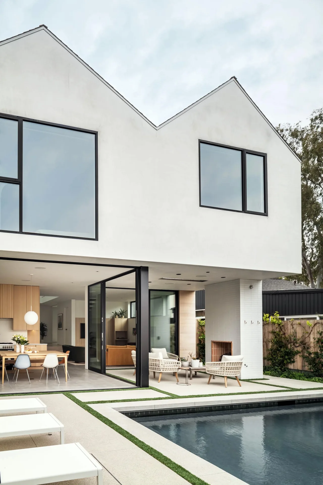 The Oak Avenue House features a minimalist white exterior with black window frames and a poolside living area with a fireplace.
