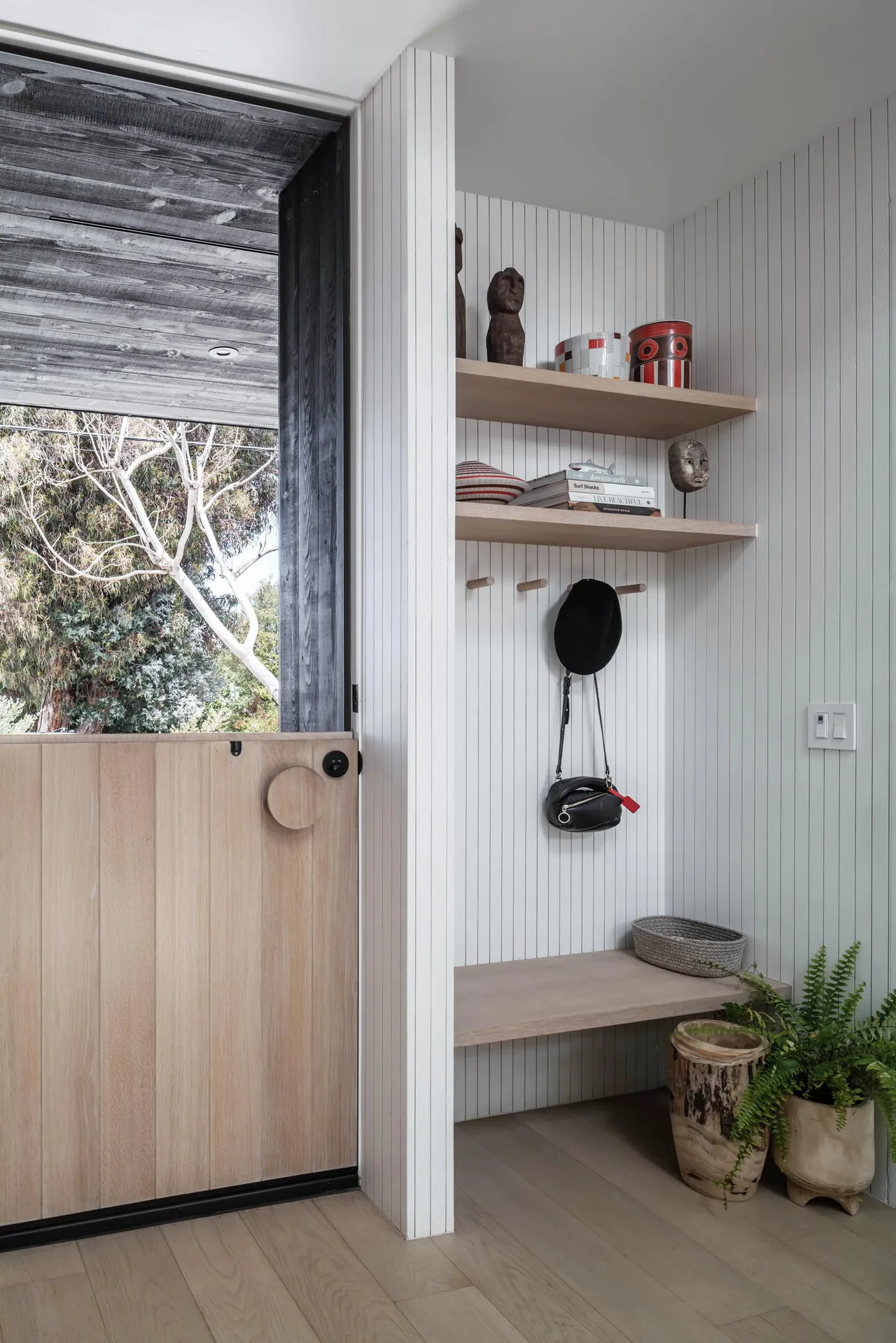 Mudroom entry area with a light wood half door, built-in bench, wooden shelves, and vertical shiplap walls.