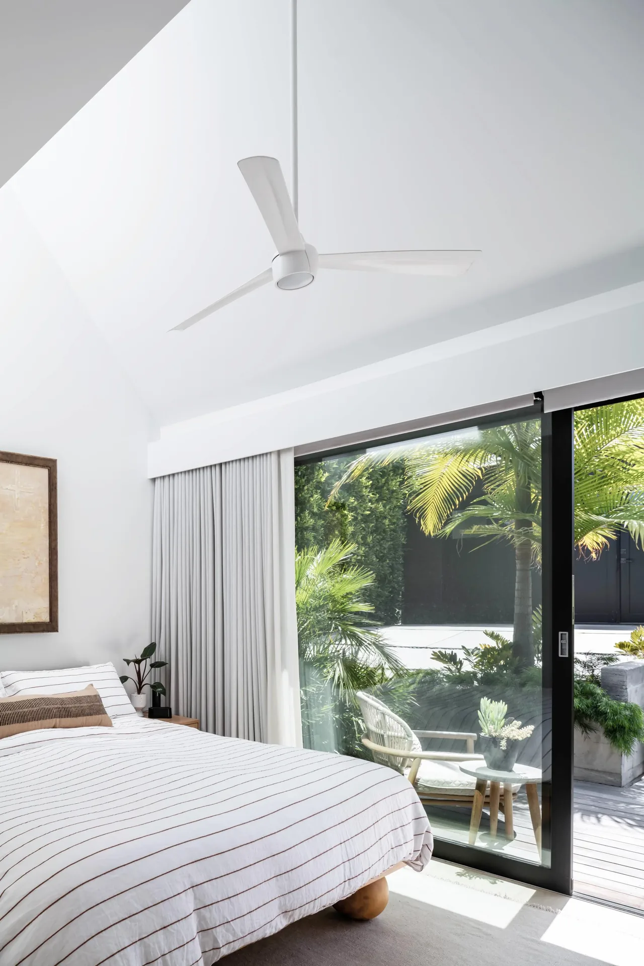 A bright bedroom features a vaulted ceiling, white ceiling fan, and sliding glass door to a green patio.