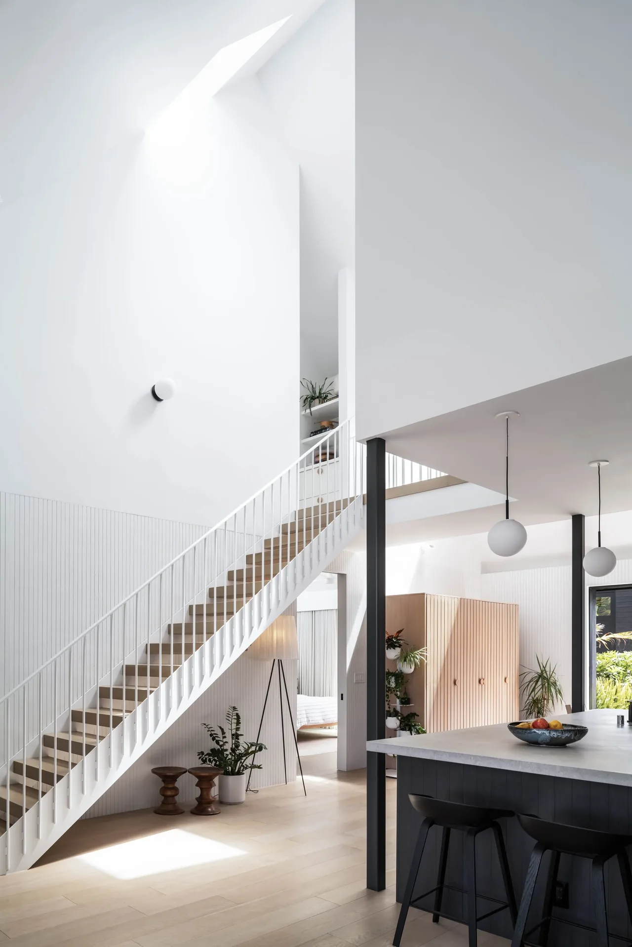 Modern living area with a staircase, kitchen island with pendant lights, and natural light from a skylight.