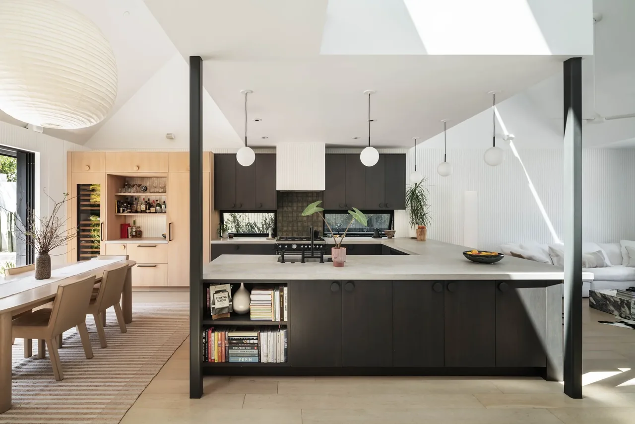 Curtis Avenue House kitchen features a large U-shaped concrete countertop island and two-tone cabinetry under vaulted ceilings.