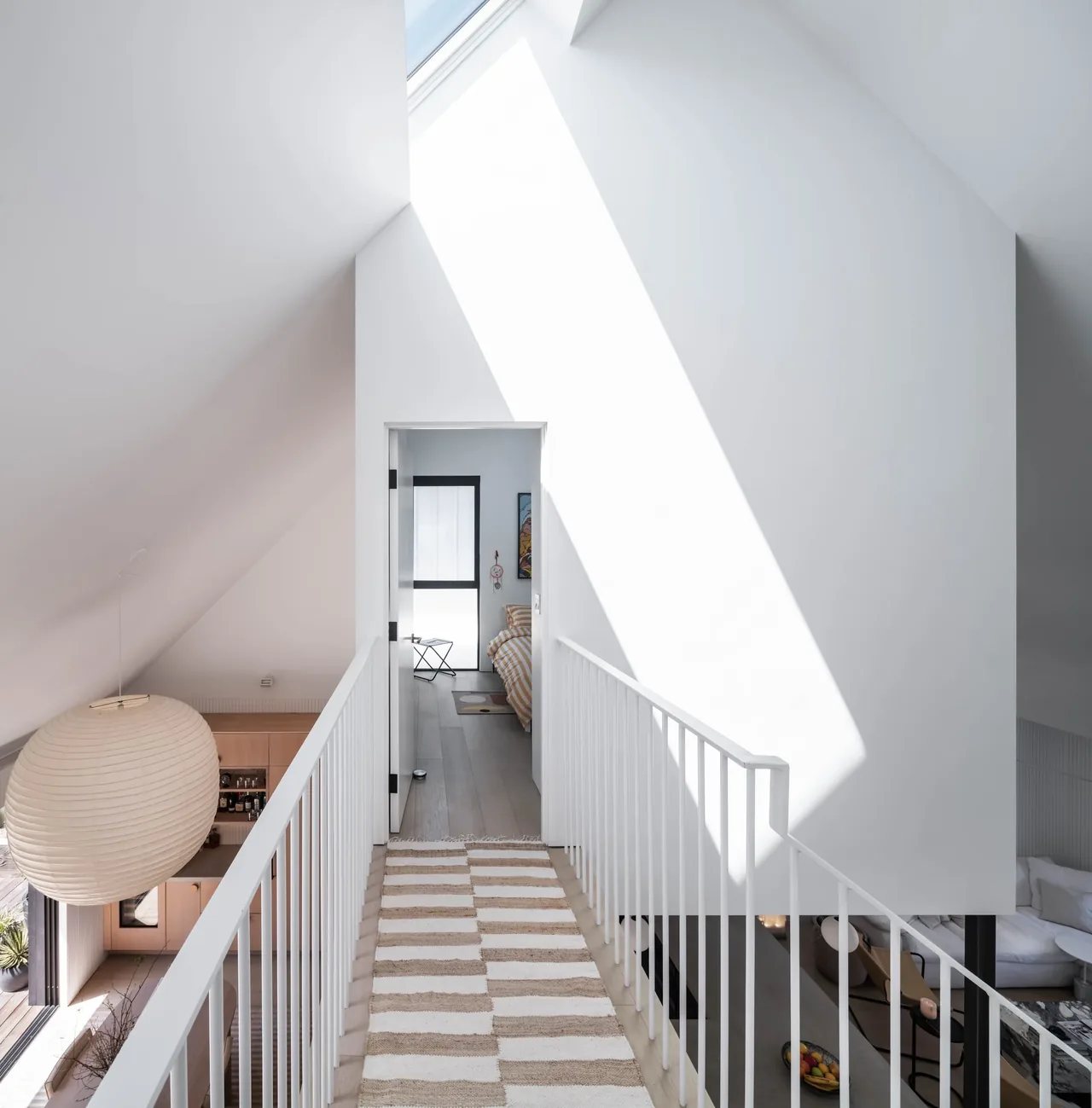 A bright upper hallway with white railings, skylight, and a view into a bedroom in the Curtis Avenue House by ras-a, inc.