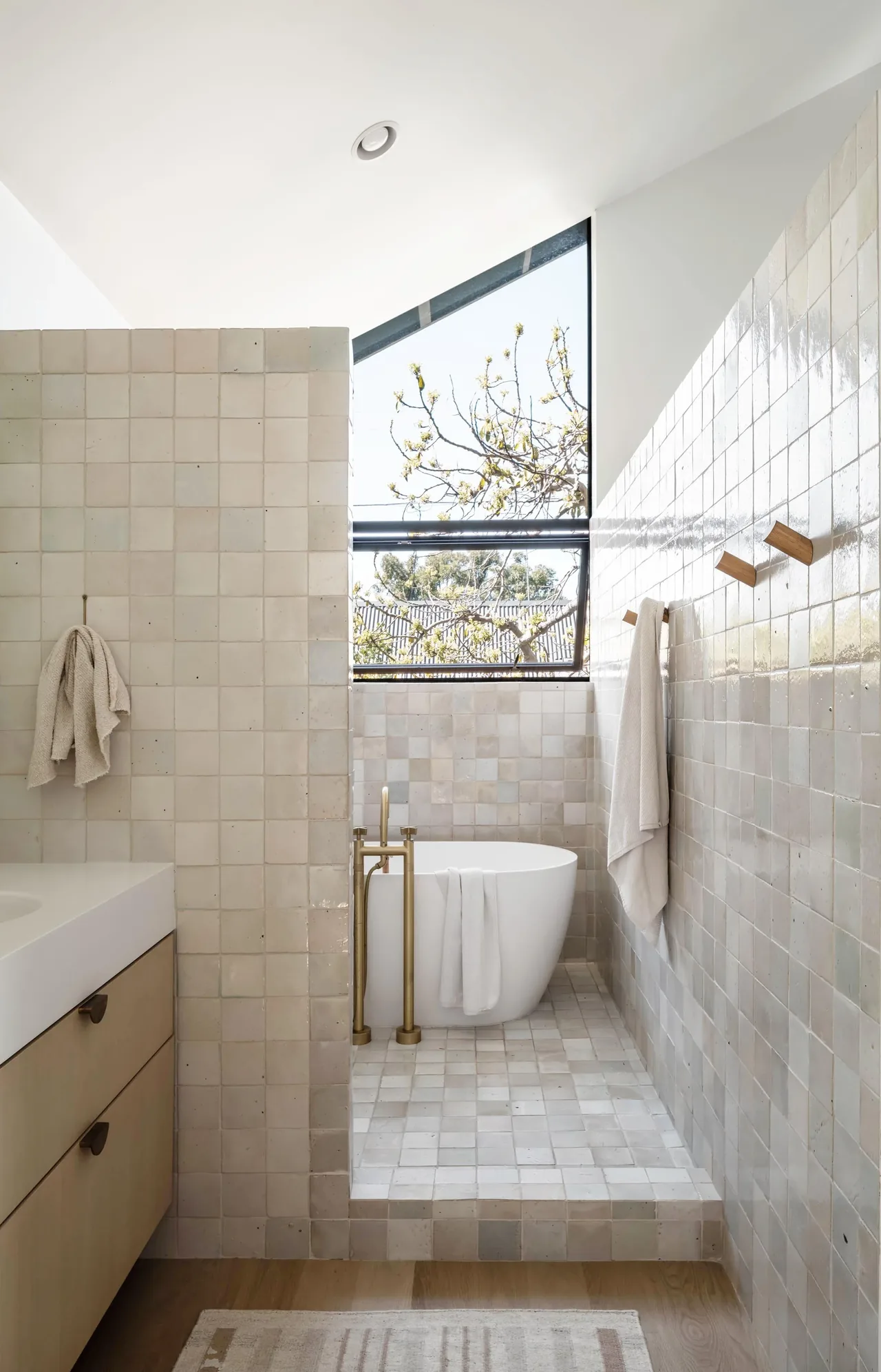 Glencoe Avenue House bathroom features a tiled soaking tub area with a large triangular window providing natural light.