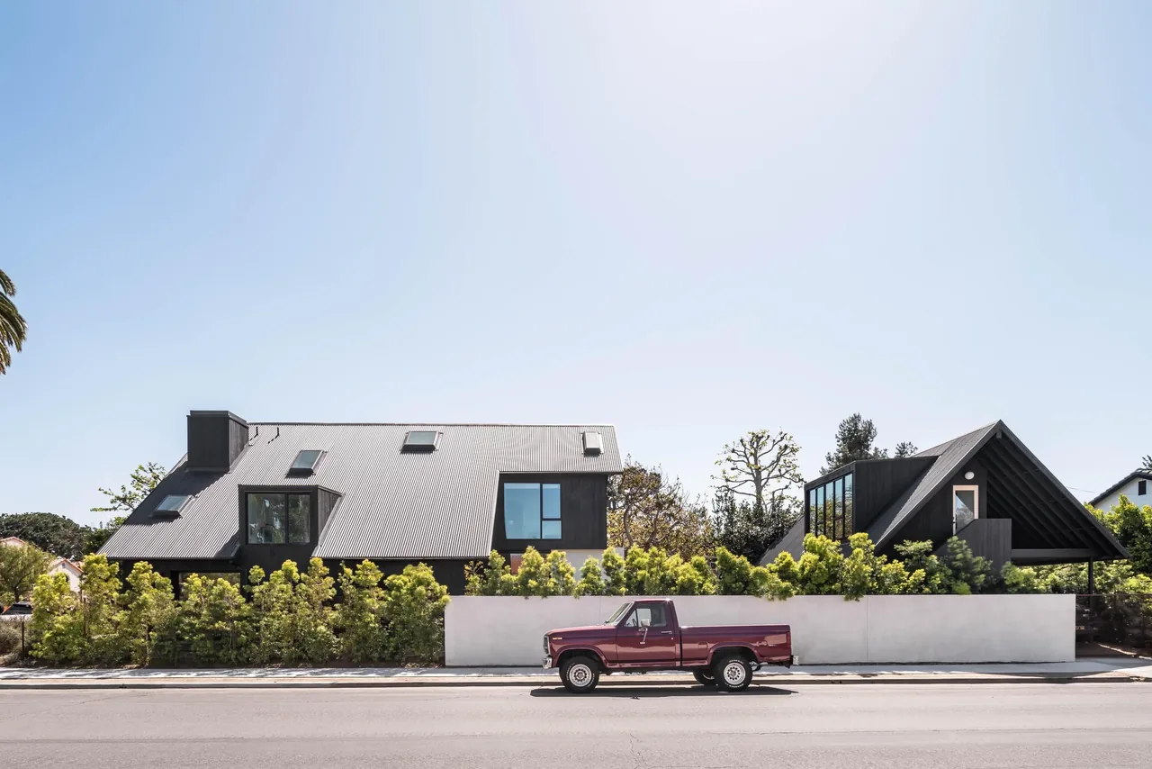 Glencoe Avenue House features a black standing seam metal roof and black window frames behind a white perimeter fence.