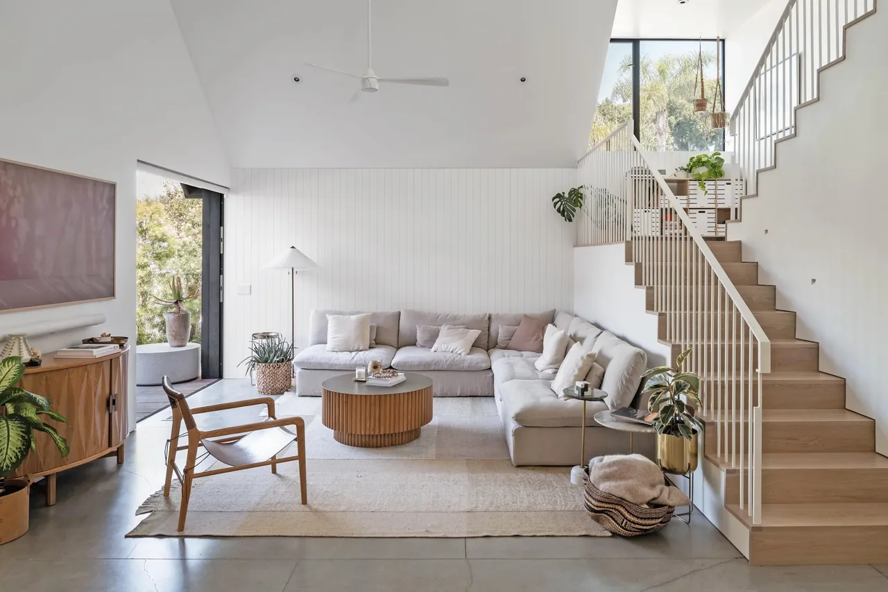 Glencoe Avenue House living room features a beige sectional sofa, wooden furniture, and a staircase with a white metal railing.