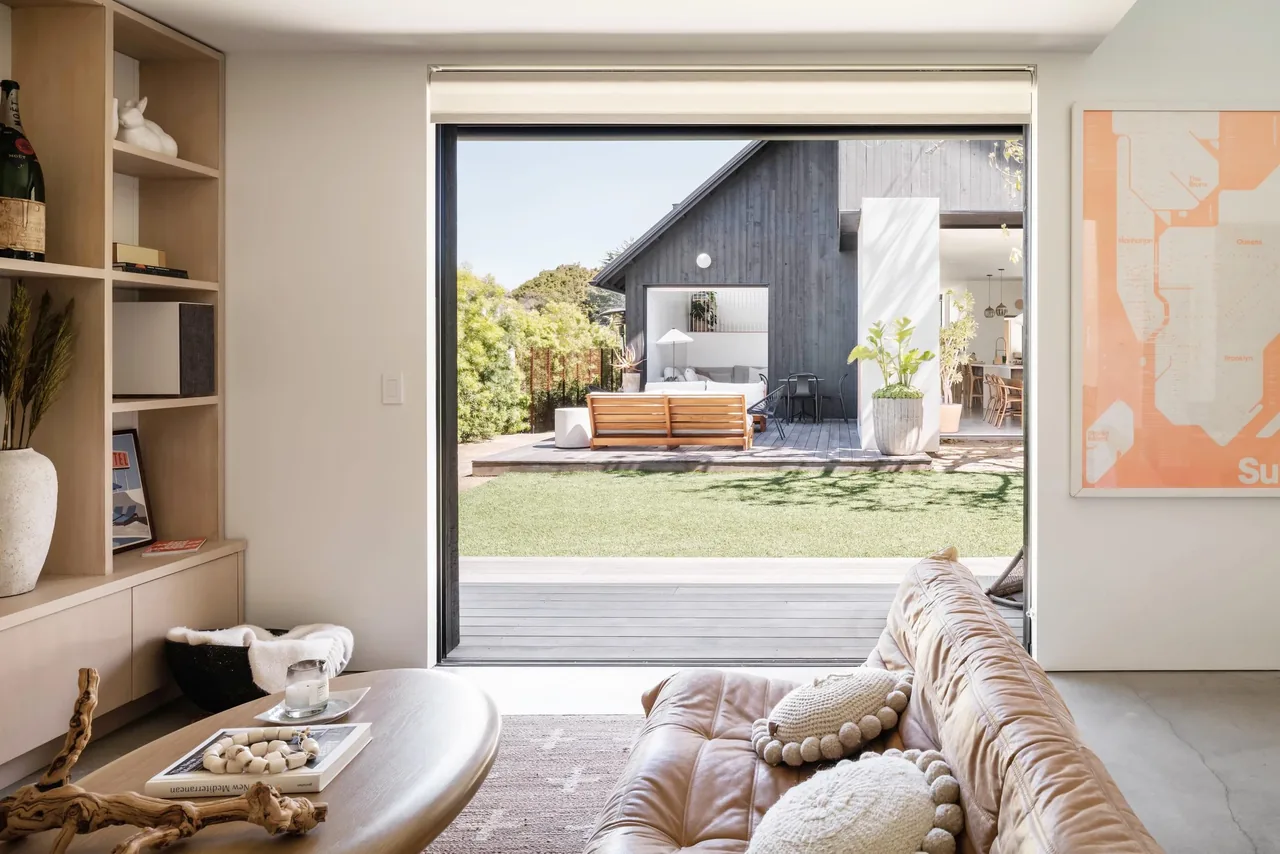 Inside the Glencoe Avenue House living room looking through large sliding glass door to an outdoor seating area and secondary building.