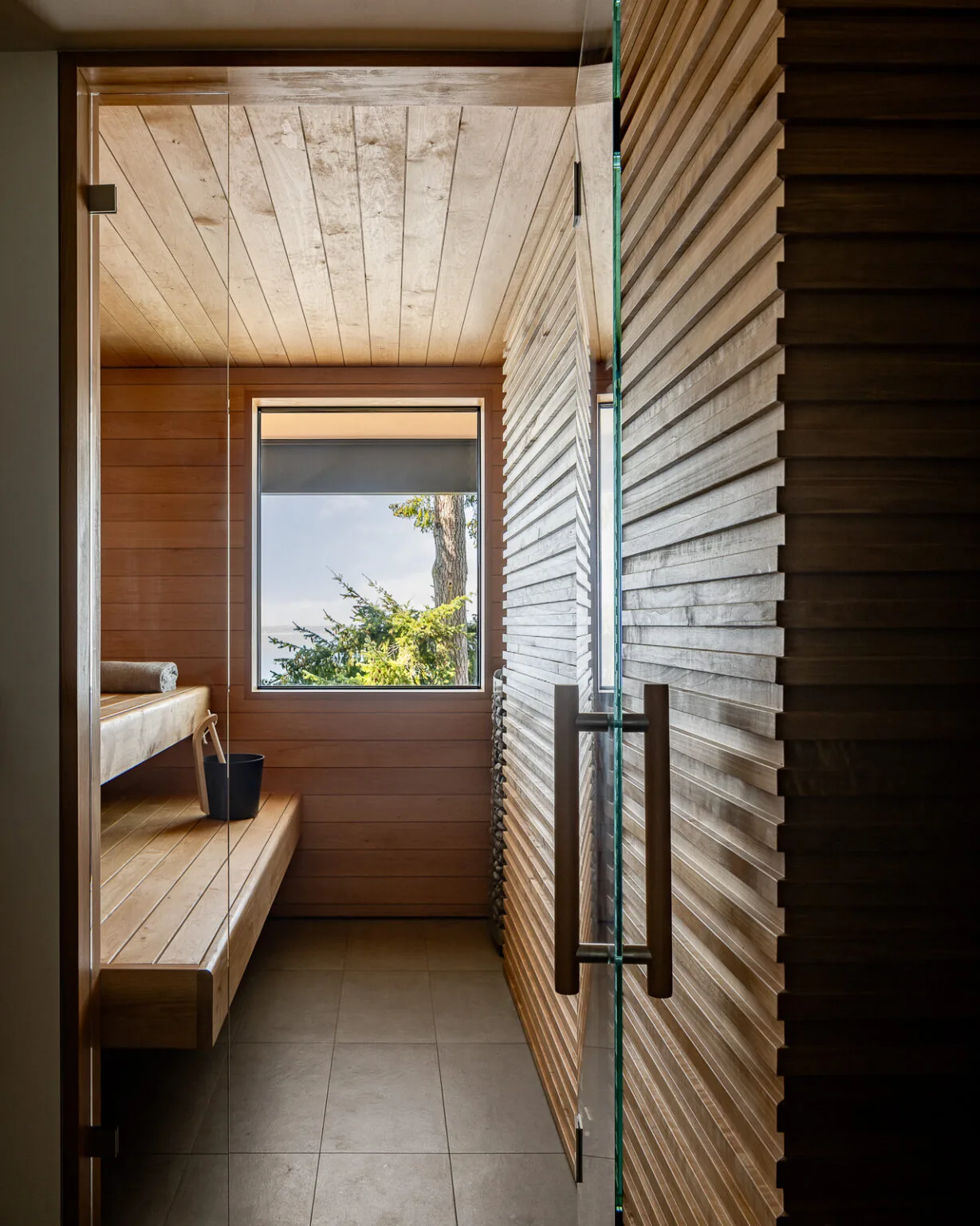 Sauna room features wood paneling, a built-in bench, and a large window with a nature view.