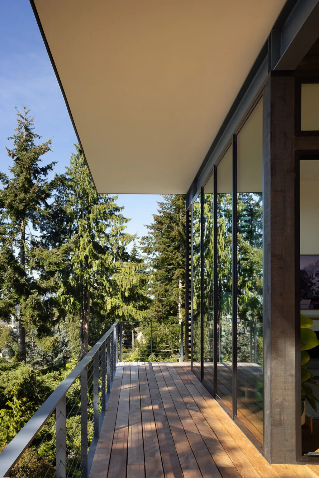 Nest project balcony by Replinger Hossner Architects with wood decking and glass railing in a forest setting.