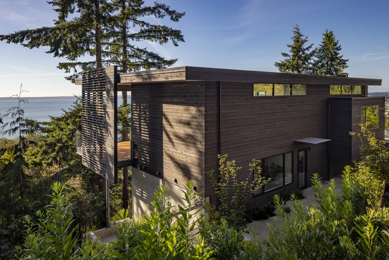 The Nest project features dark wood siding, clerestory windows, and a slatted wood screen on a modern residence with water views.