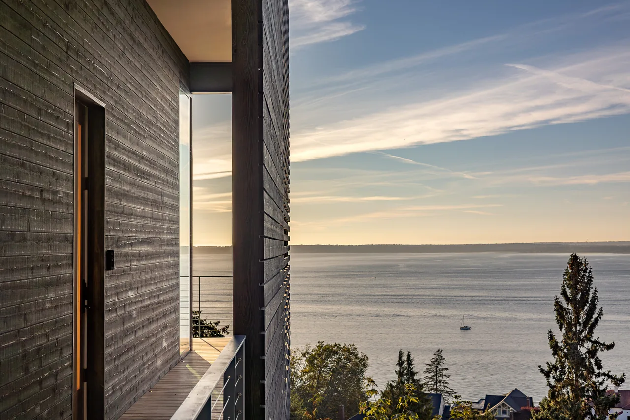 Balcony view from Nest project featuring black wood slat exterior walls and cable railing facing a water view at sunset.