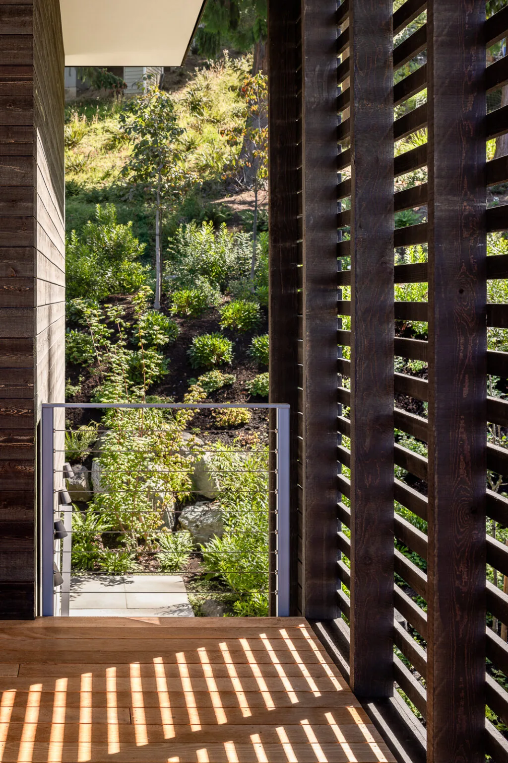 Nest project features a wooden balcony with vertical slatted wood screens and a cable railing overlooking a green hillside.