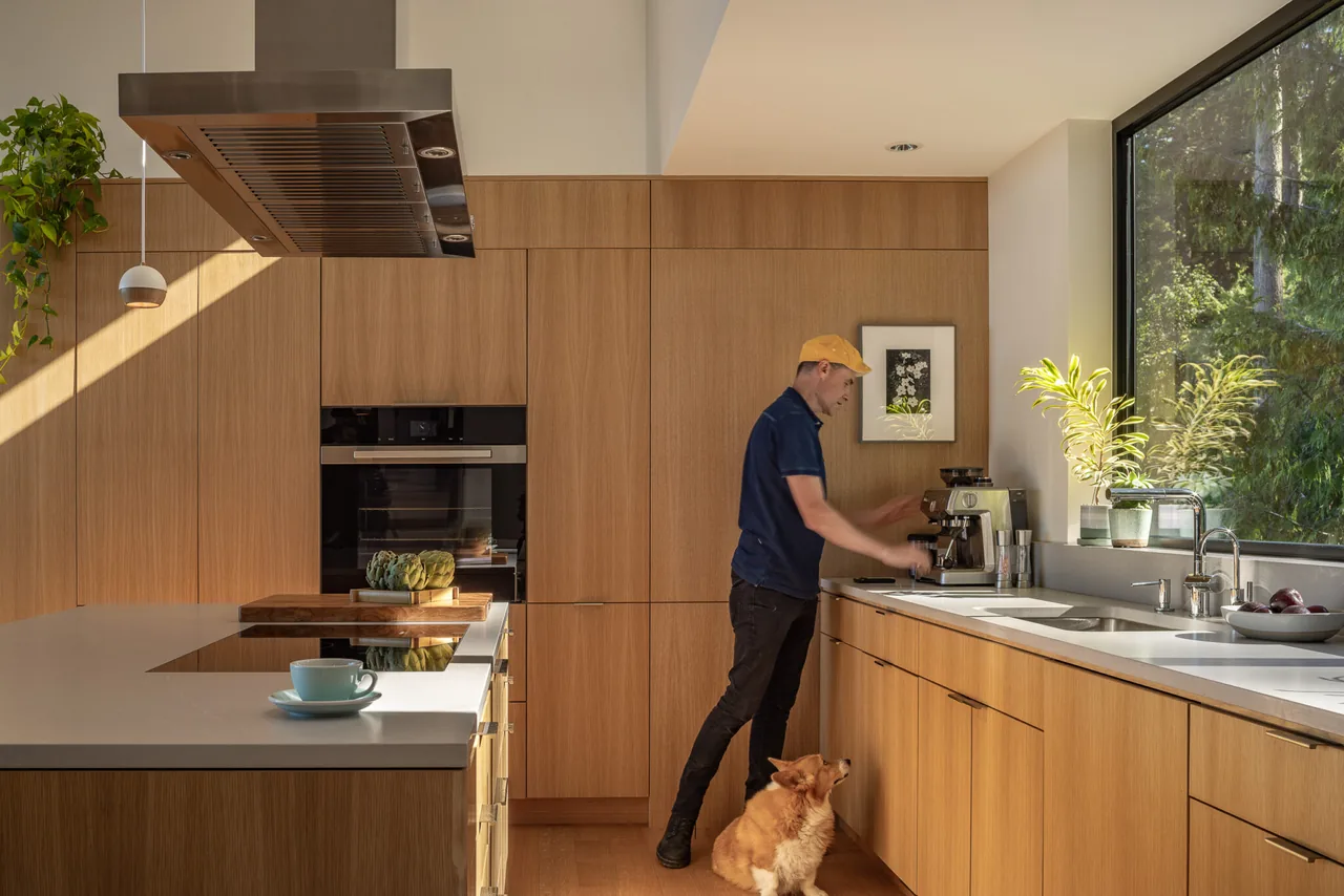 Modern kitchen with wood cabinetry and a large forest-view window in the Nest project by Replinger Hossner Architects.