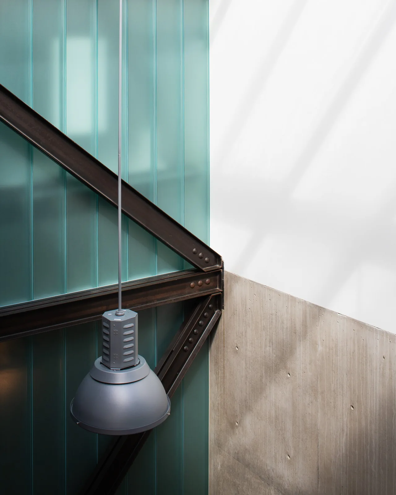 Interior view showing a pendant light, exposed steel beams, frosted glass wall, and a concrete wall in the DMG House.