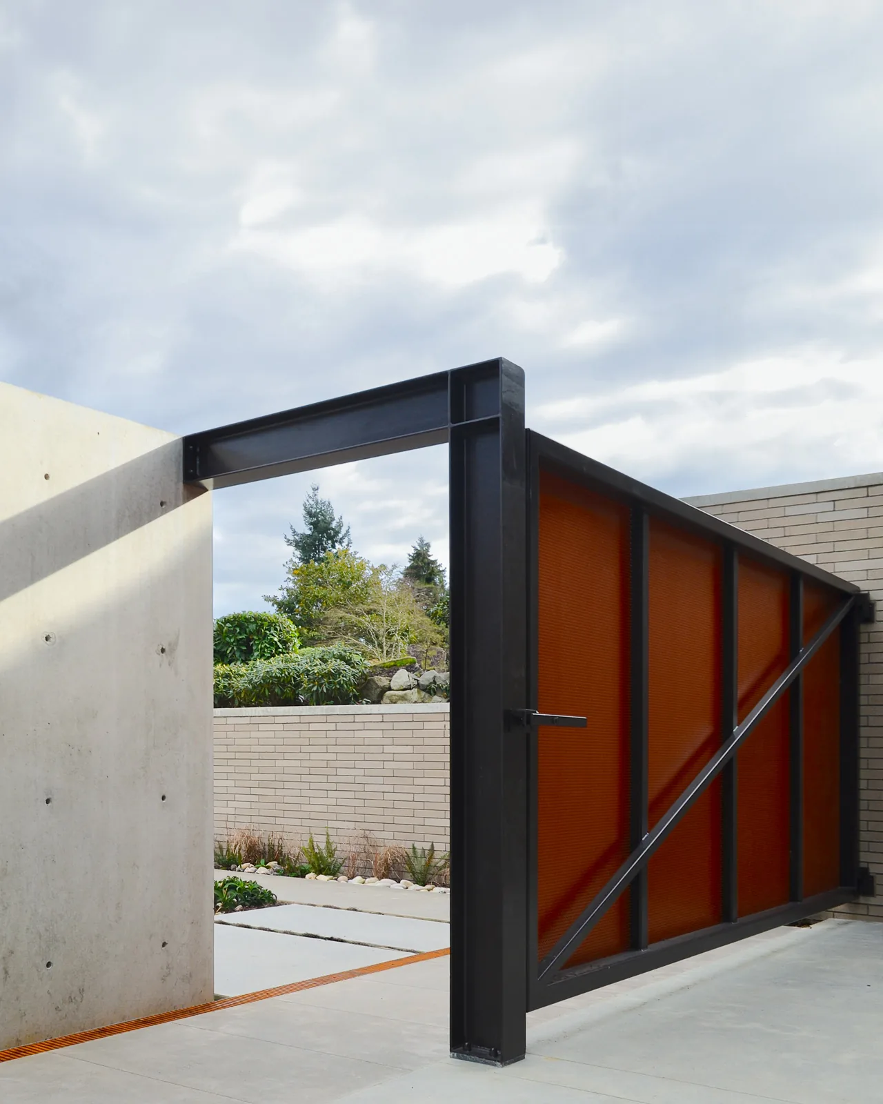 Swinging metal gate with rust-colored panels opens from concrete wall to outdoor area.