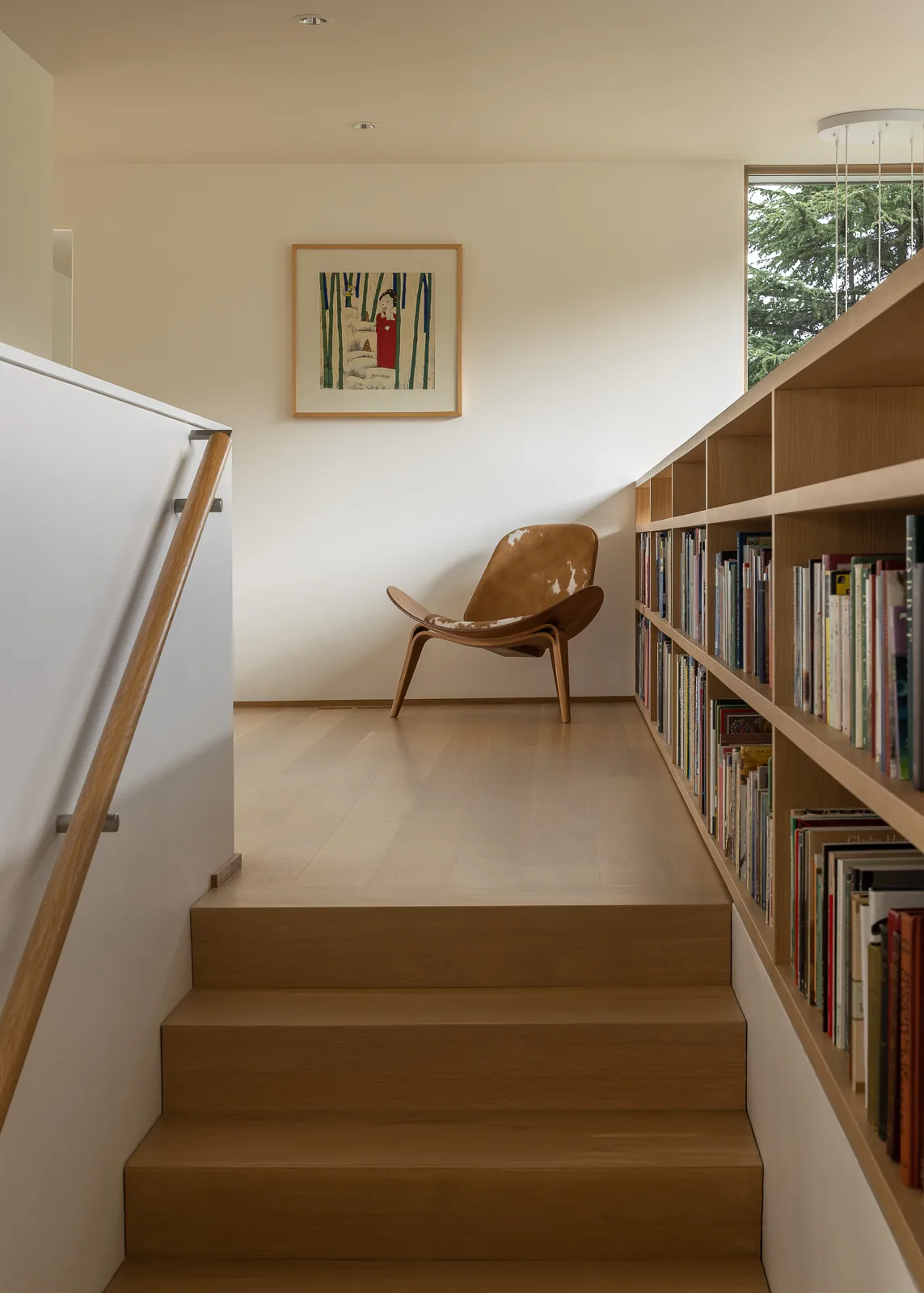 Stair landing with built-in bookshelf, leather chair, and framed artwork in a residential setting.