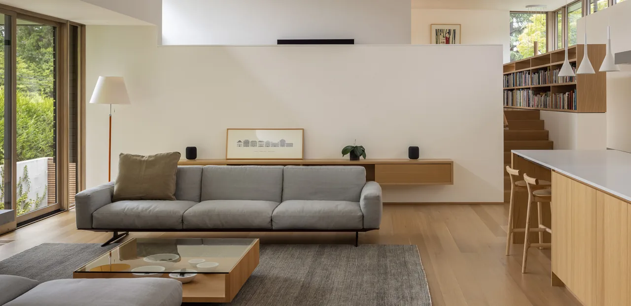 MADISON project by Replinger Hossner Architects shows a living room with gray sofa and kitchen island with wood cabinetry.