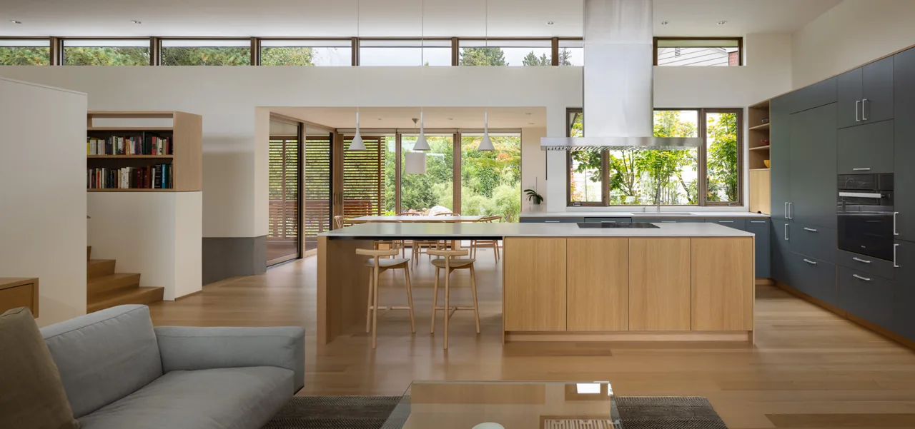 Modern kitchen with wood and gray cabinetry, large island, and natural light from clerestory windows overlooking garden greenery.