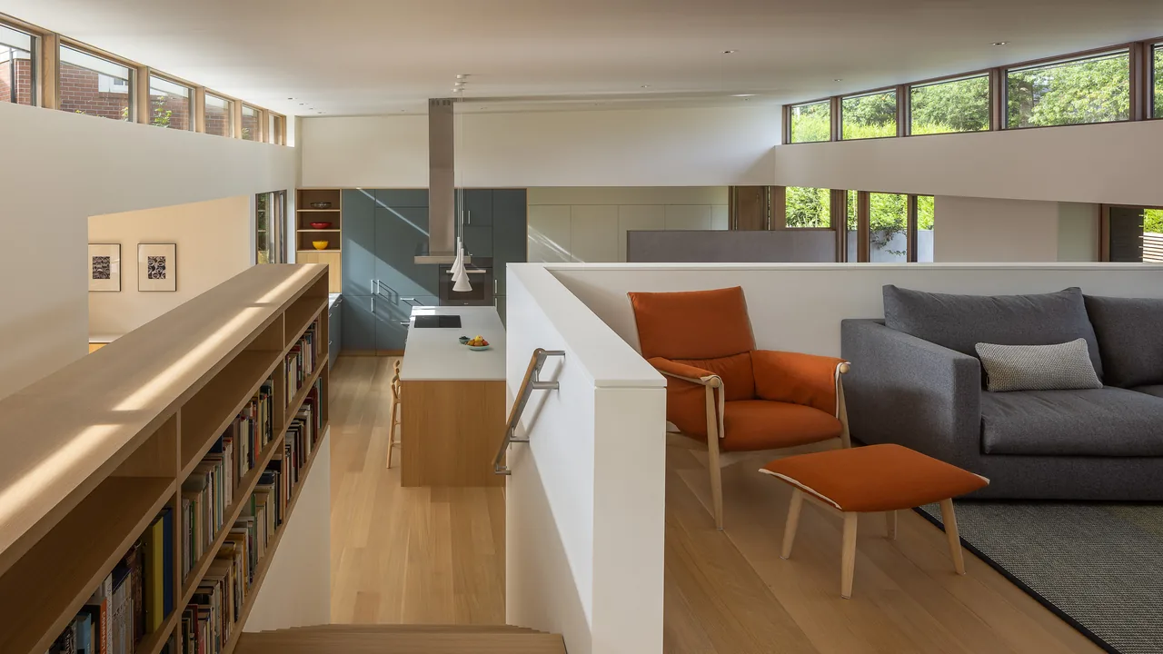 Modern open living space with natural light from clerestory windows, wood cabinetry, and cushioned lounge chair with ottoman.