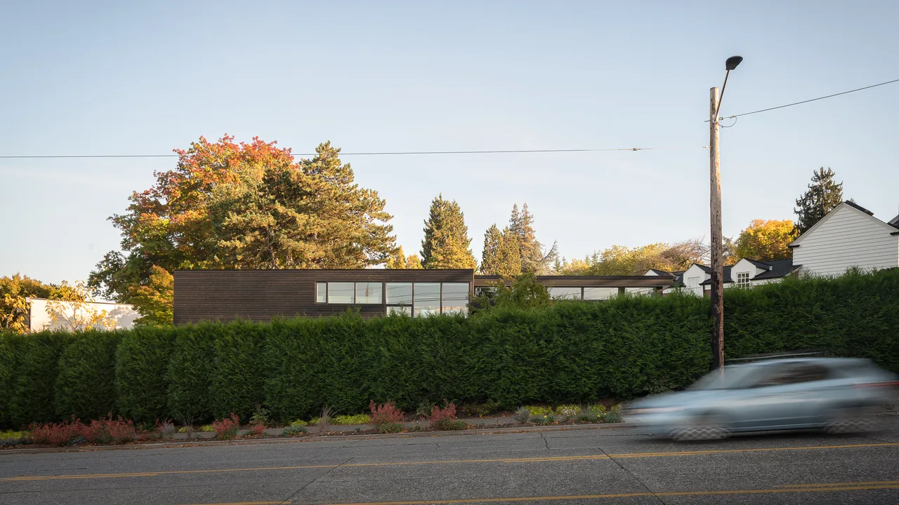 The MADISON project features a modern house with horizontal wood siding partially obscured by dense hedge greenery.