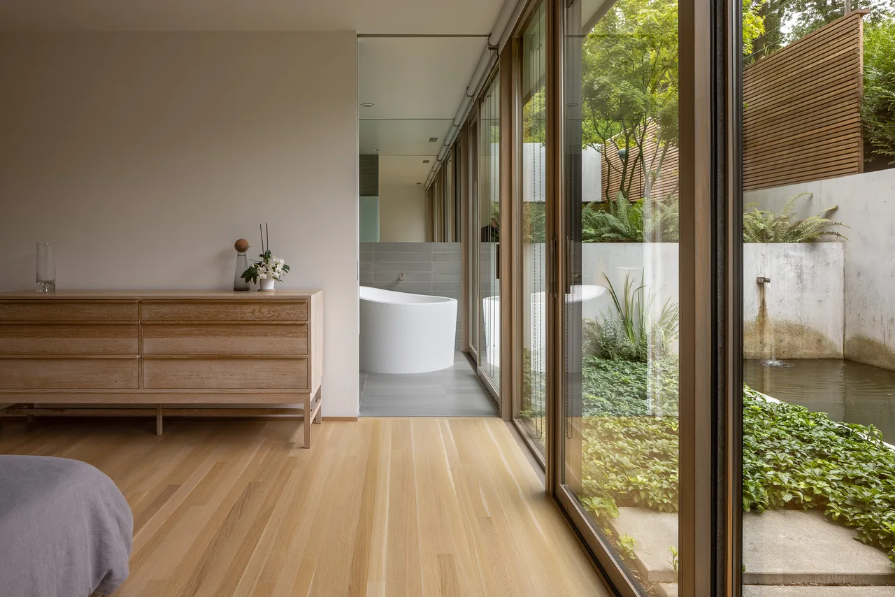 Bedroom with wooden dresser and floor-to-ceiling glass doors opening to a landscaped outdoor pond area.