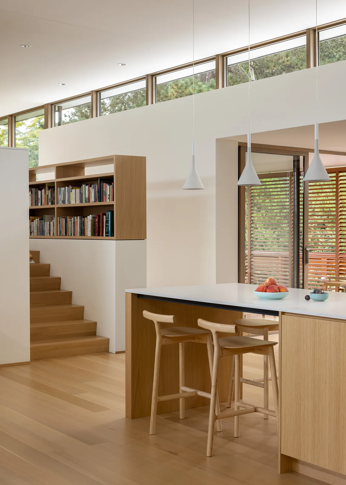 MADISON house features a kitchen island with wooden stools and integrated bookshelf near elevated windows and sliding door.