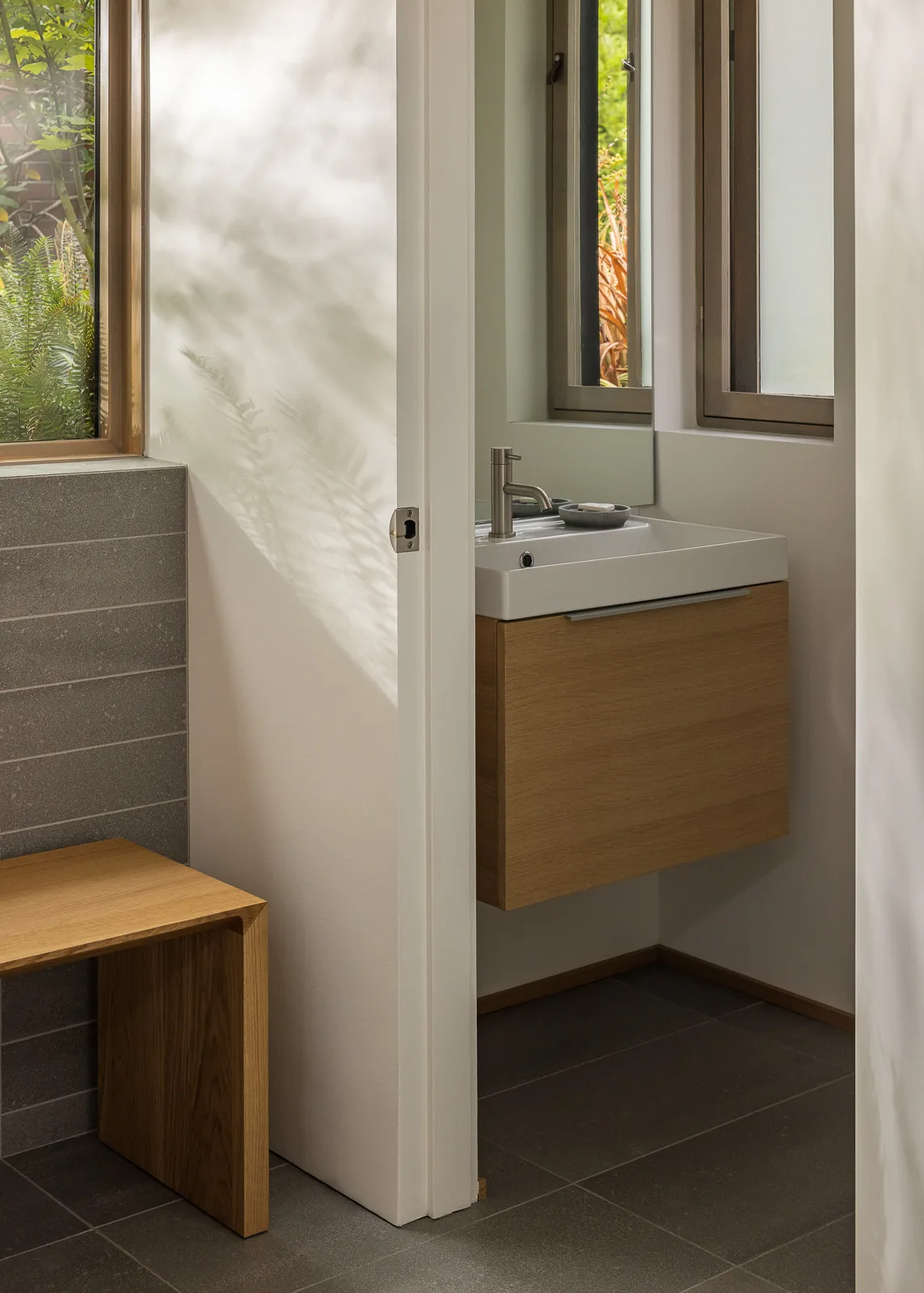 Small bathroom featuring a floating wooden vanity with a white sink and faucet, alongside two windows.