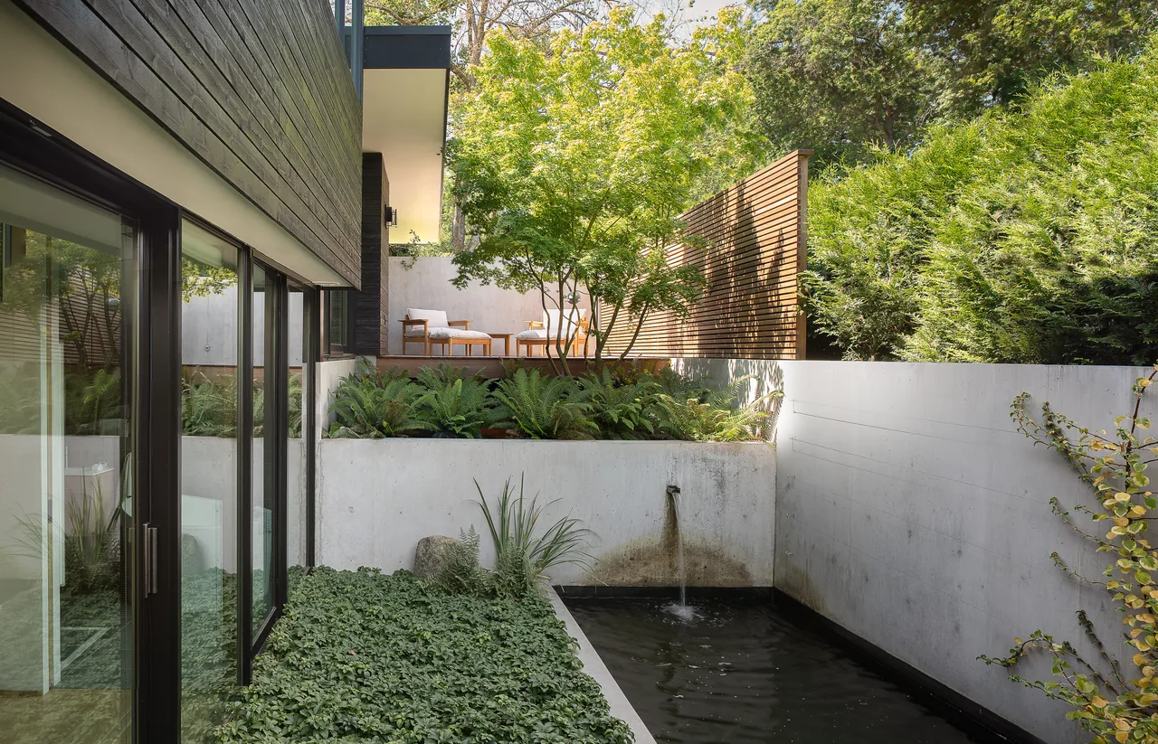 Outdoor living space features a concrete water wall pool, raised wooden deck with lounge chairs, and wood privacy fencing.