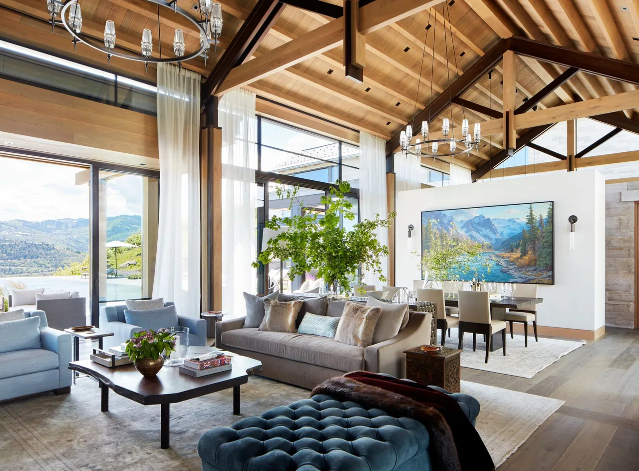 Living area with vaulted wood ceiling and large glass walls overlooking mountain scenery and pool.