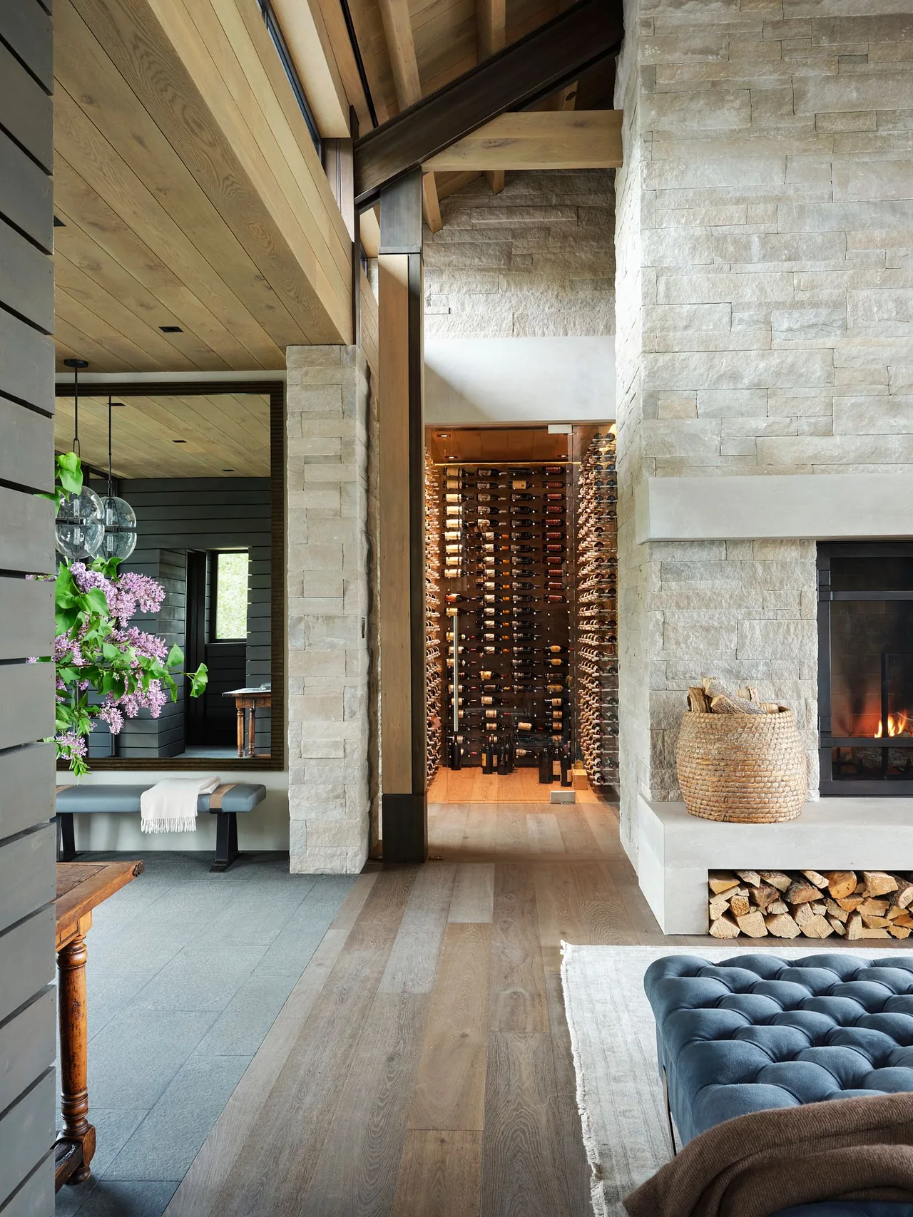 Living area with stone fireplace, wood ceiling, and illuminated wine storage in Morning Star Residence by Poss Architecture + Planning.