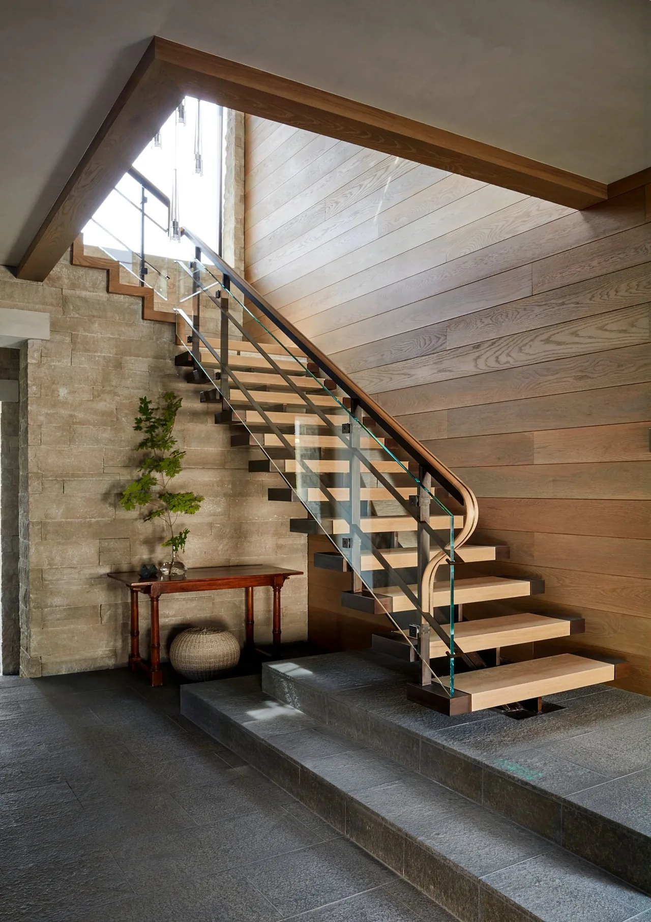 Floating stair with glass and metal handrail in the Morning Star Residence entry, featuring stone and wood-paneled walls.