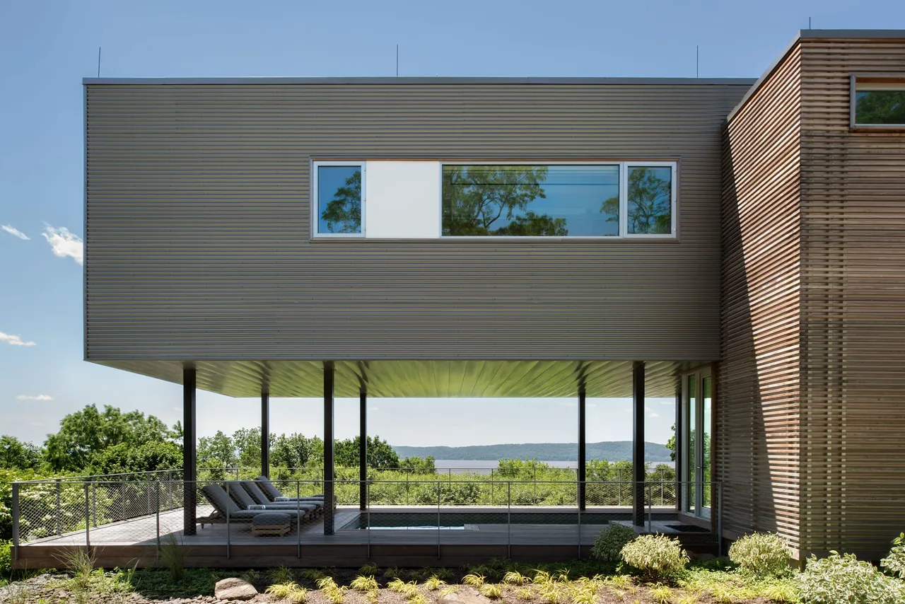 Hudson River House by Resolution 4 Architecture features a cantilevered upper floor over a covered patio with views of the river and hills.