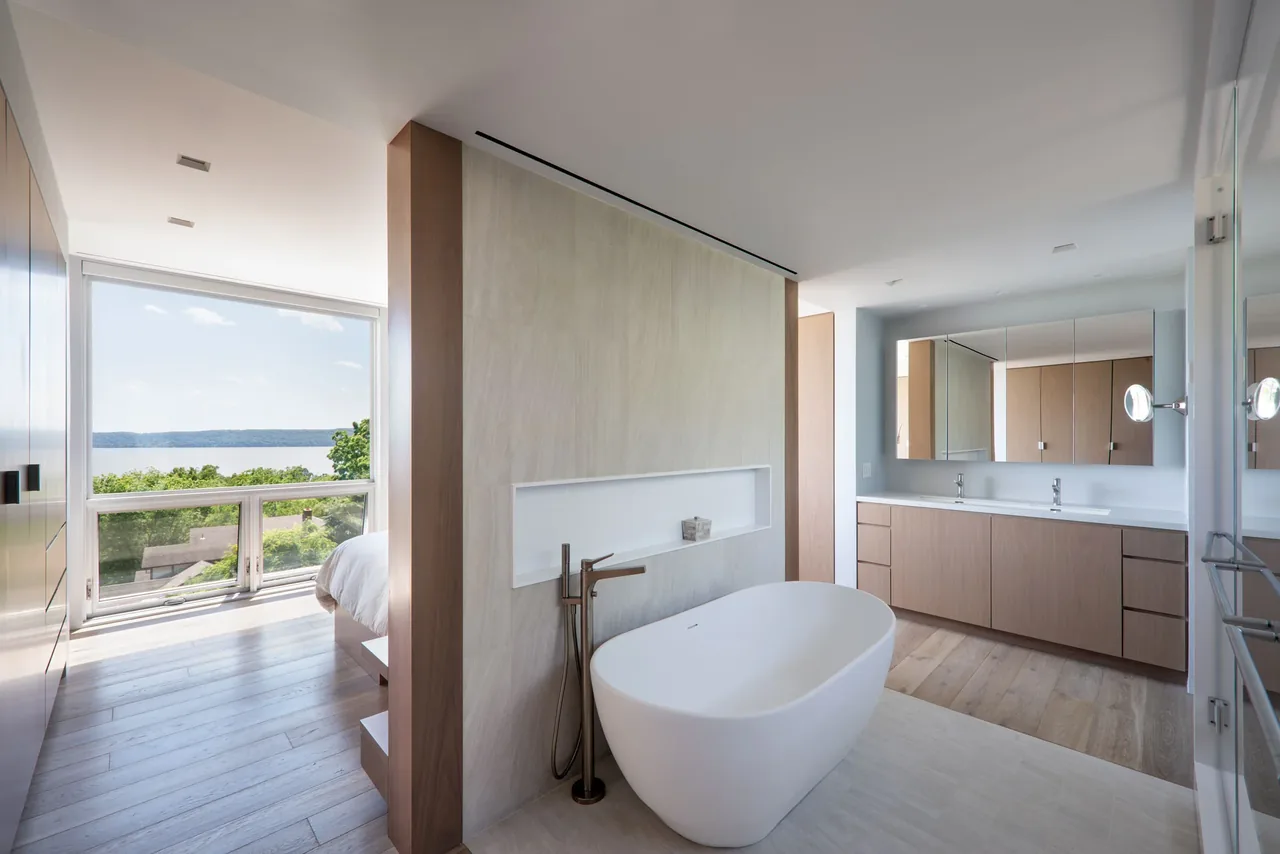 Bathroom features a freestanding tub and double vanity with large windows offering a river view.