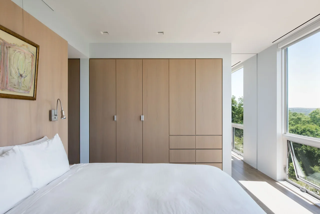Modern bedroom in Hudson River House featuring large windows and minimal wood cabinetry.