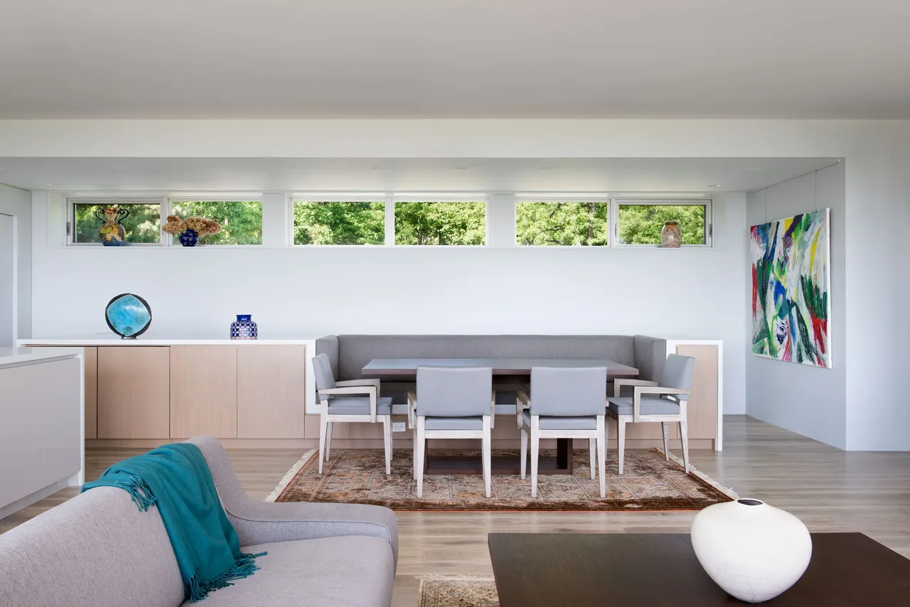 Dining space features a built-in bench, gray chairs, wooden floors, and clerestory windows bringing natural light.