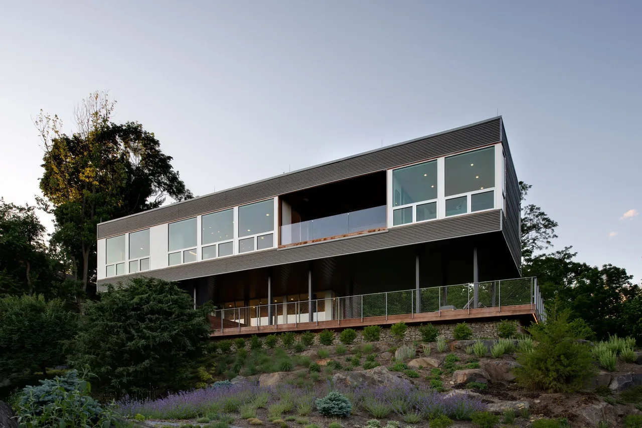 Hudson River House features elevated living space with large horizontal windows and a deck overlooking landscaped grounds.