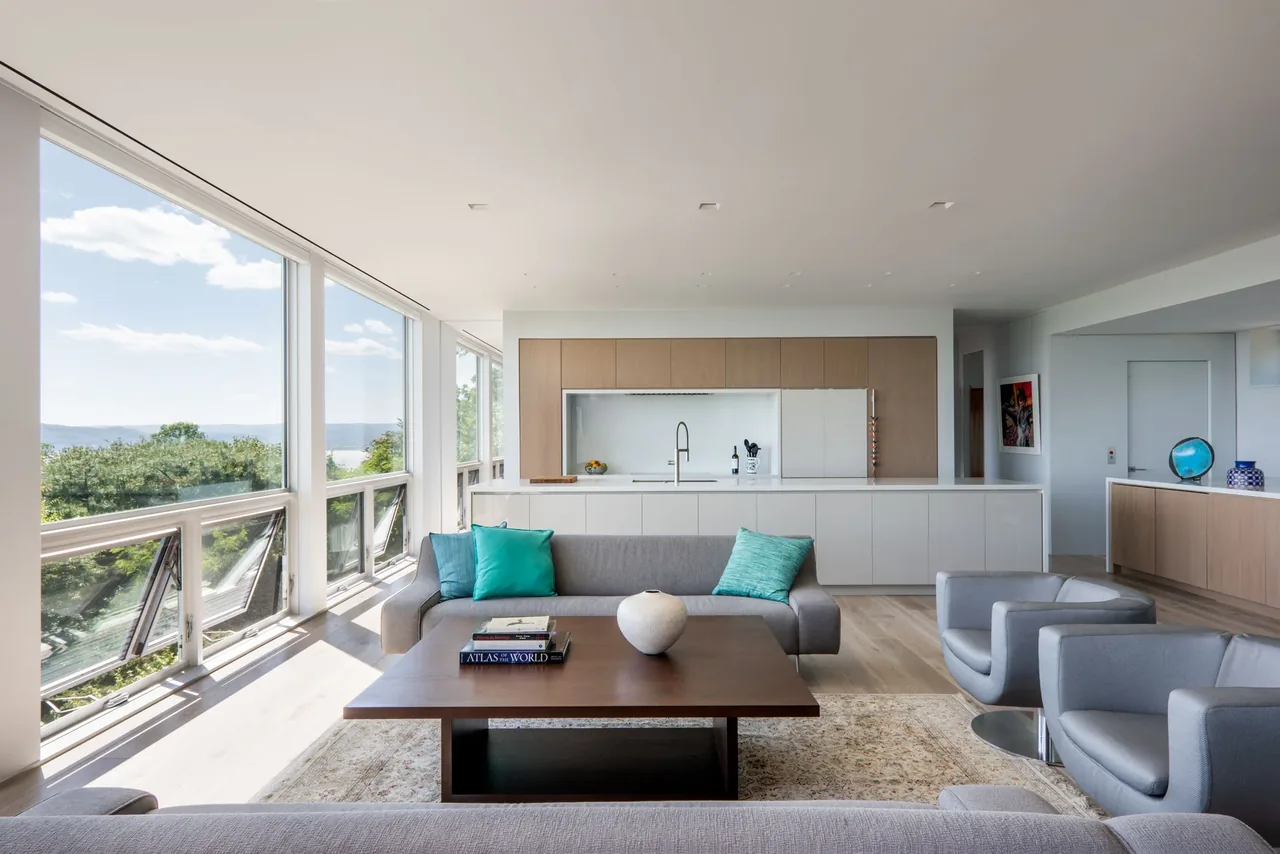 Living room with large floor-to-ceiling windows offering a river view and a contemporary kitchen in the background.