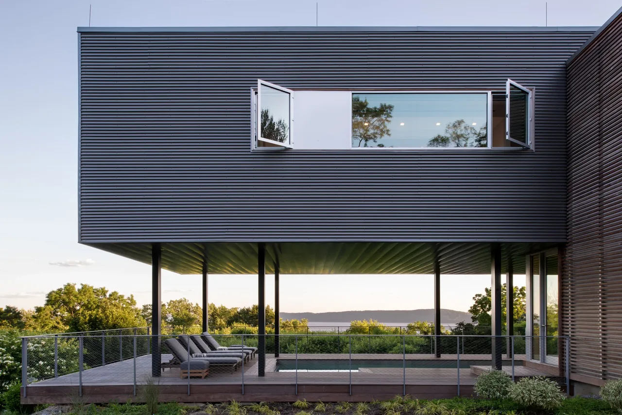 The Hudson River House features an elevated living space with a horizontal window band and an outdoor deck with lounge chairs facing a river view.