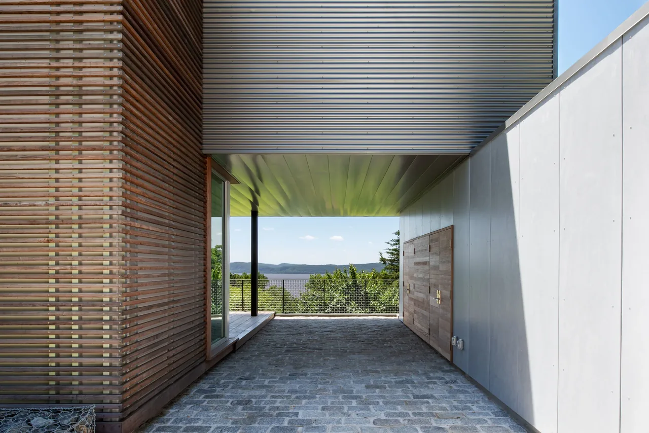 The Hudson River House features a covered outdoor passage with wood slatted paneling and metal cladding, overlooking a river view.